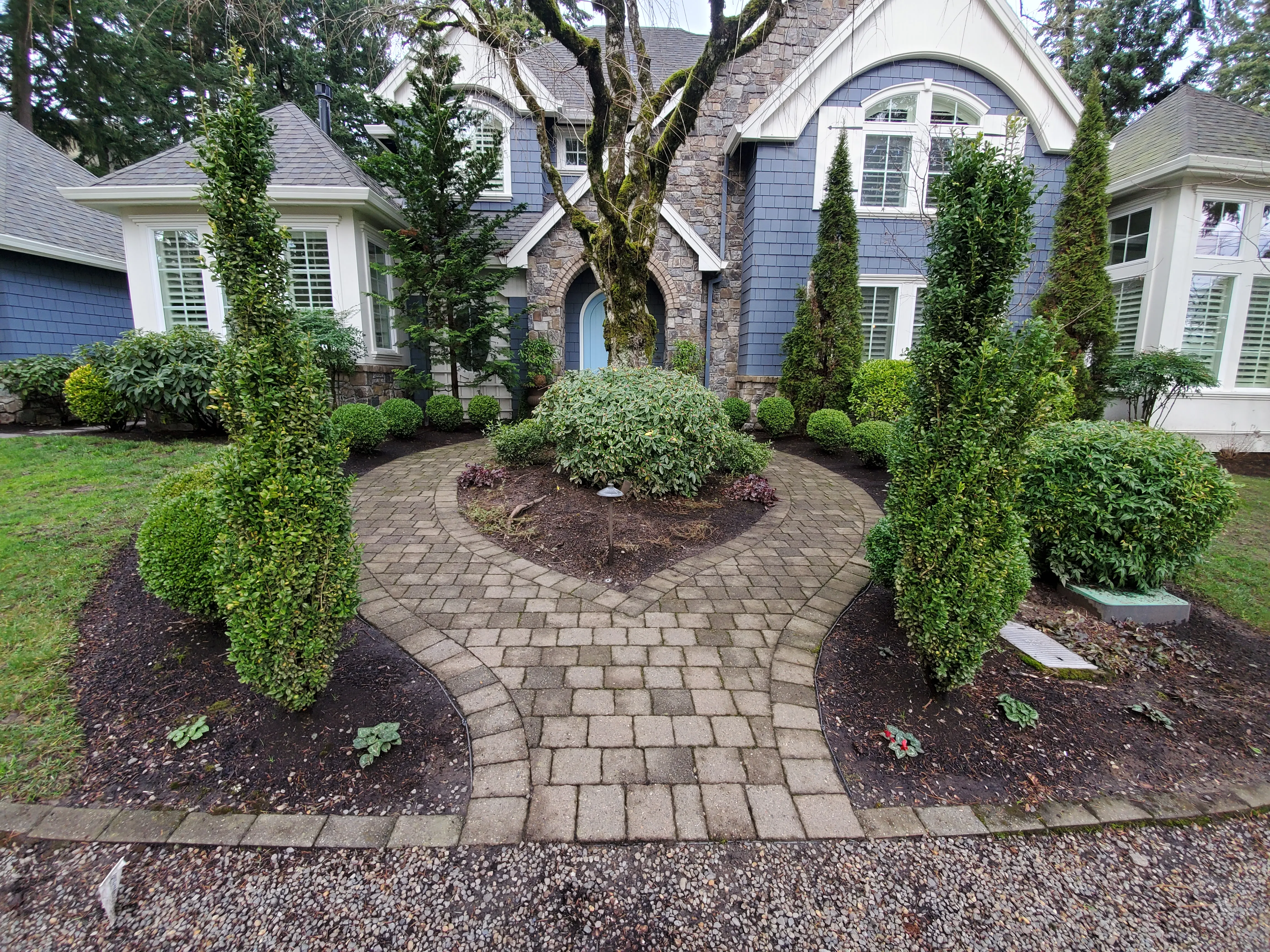 Paver entry walk in winter with bare mulch beds and an empty center island