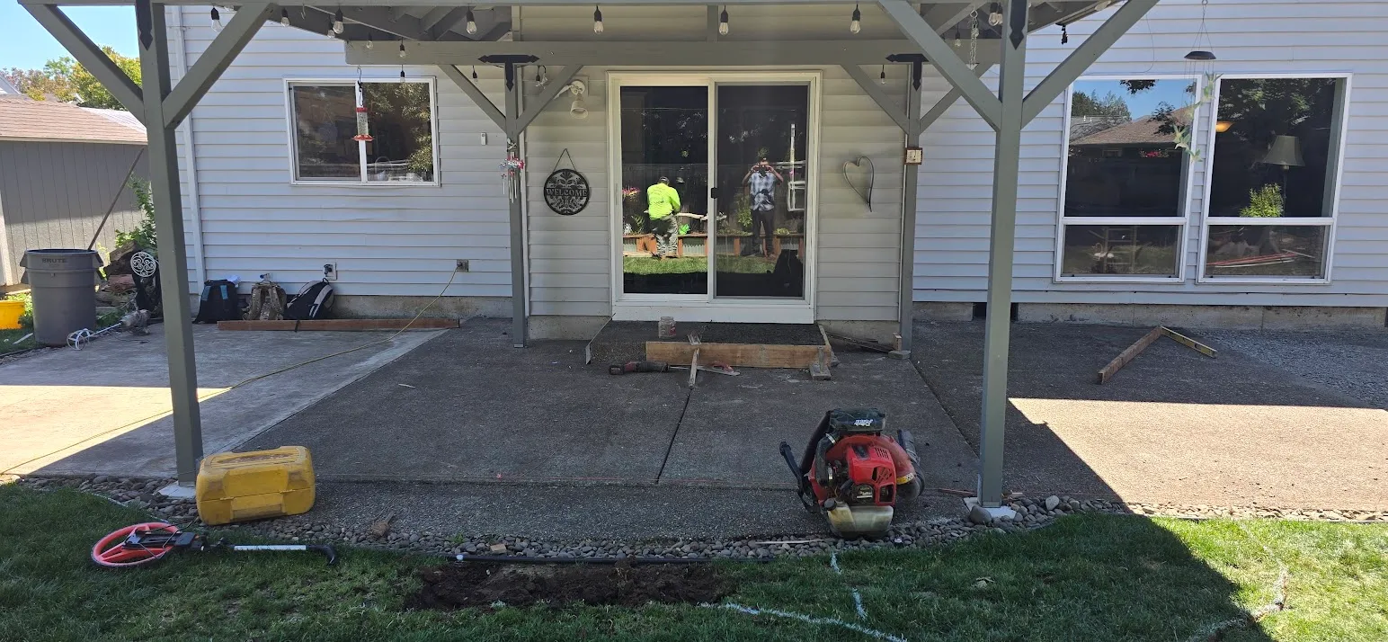 Worn concrete patio under a covered porch with forms being set at the door