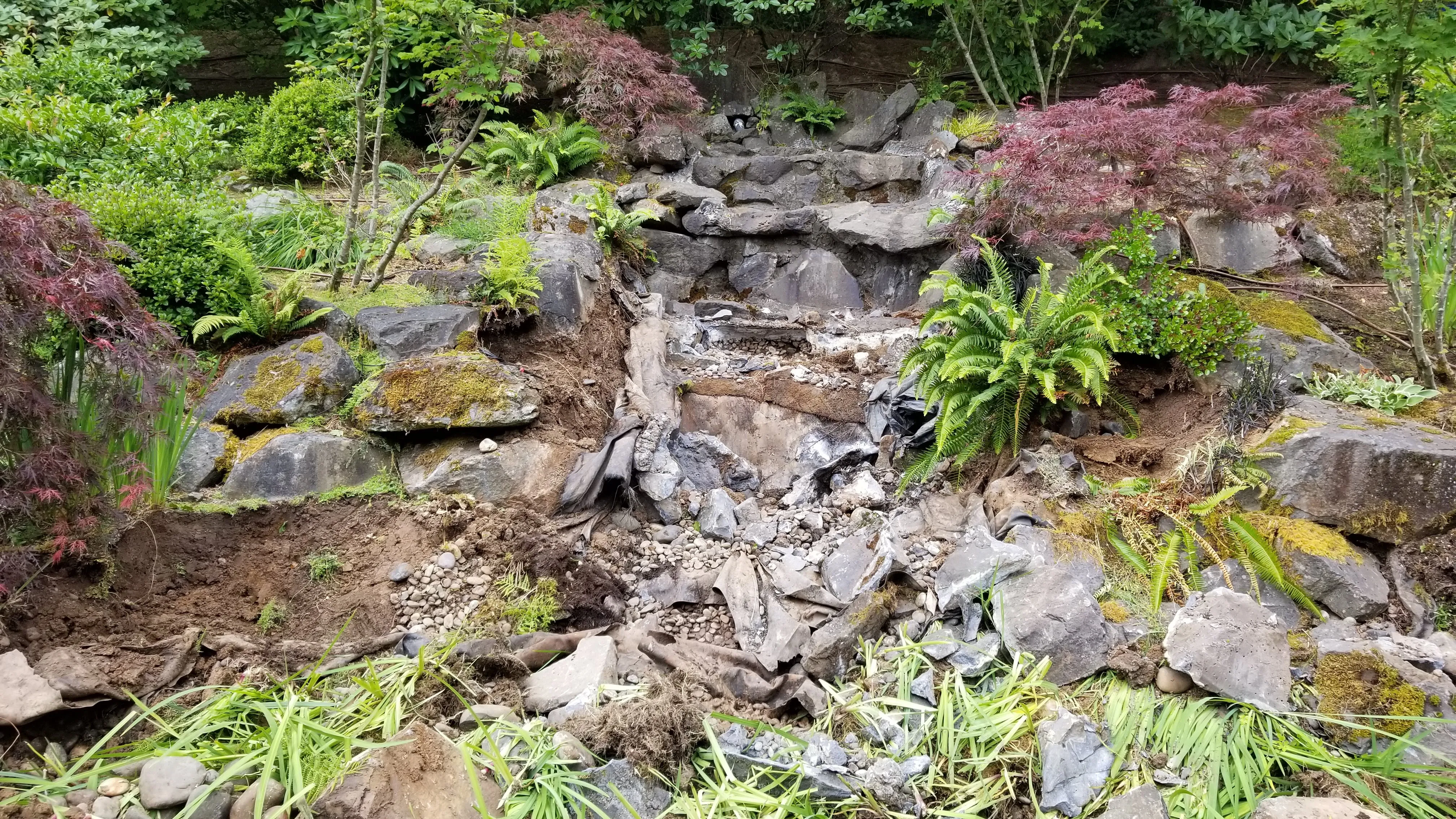 Old hillside waterfall stripped for rebuild, worn liner and displaced rock exposed