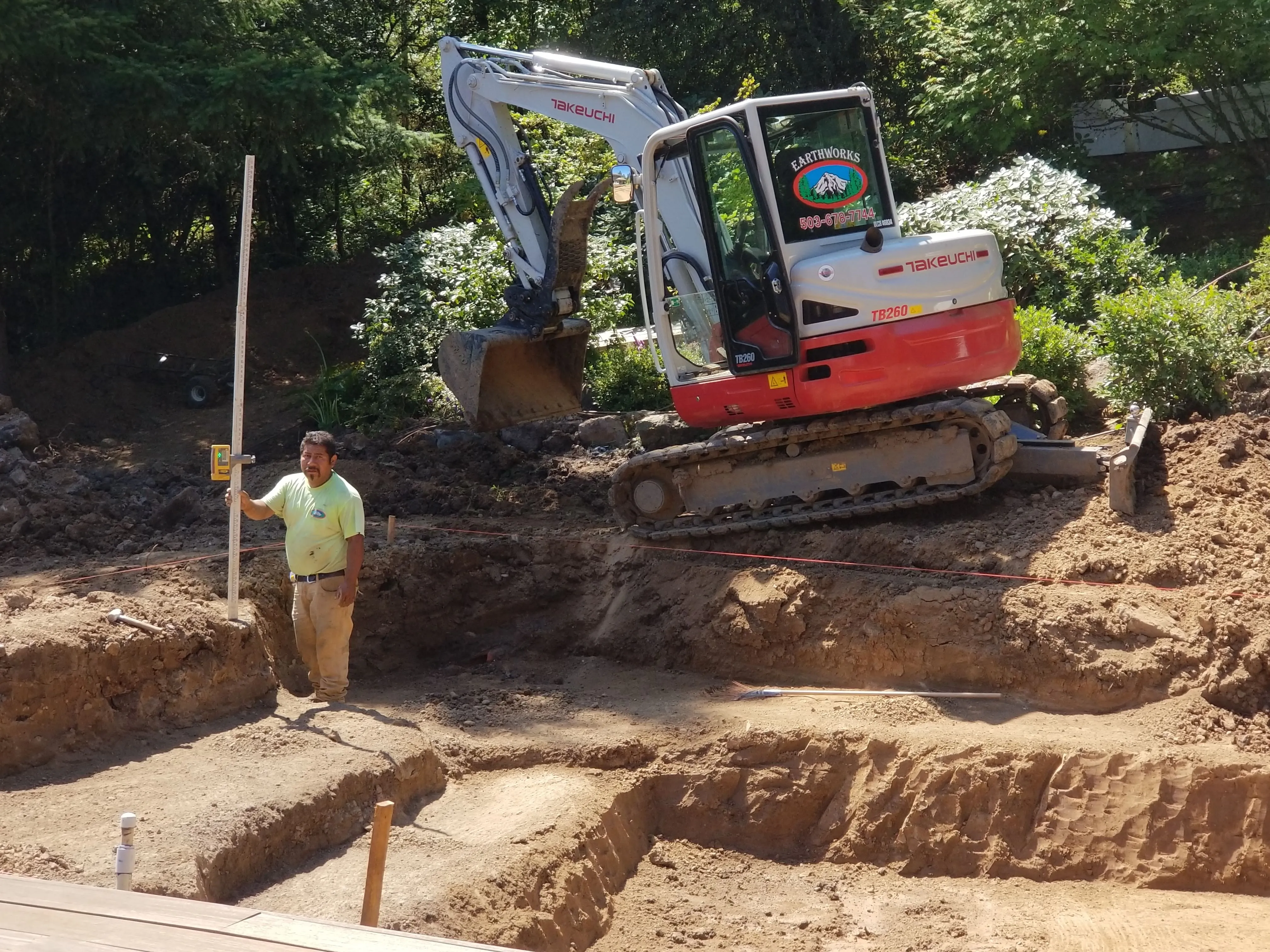 Mini excavator carving the terraced pond basin into bare earth