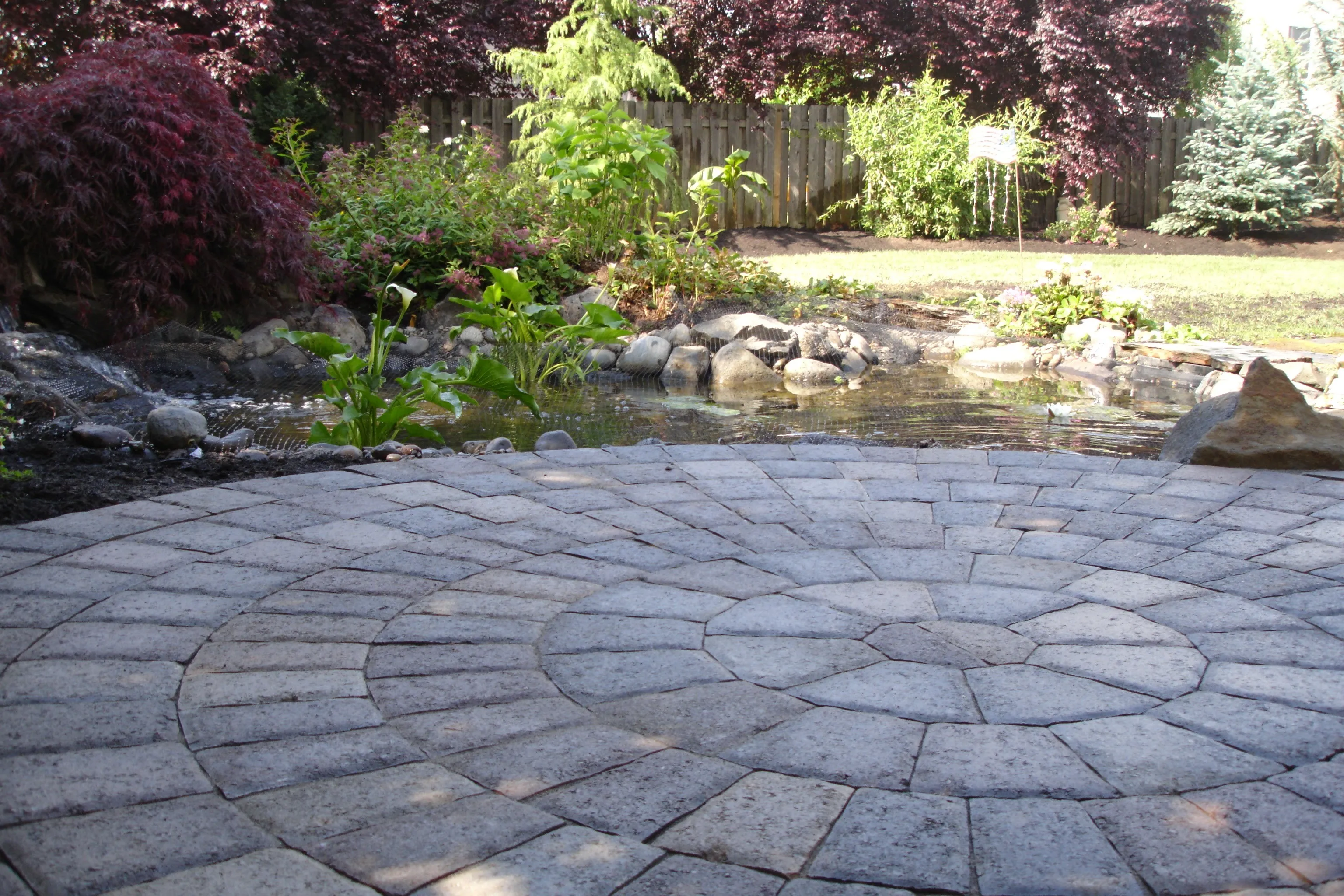 Circle-pattern paver patio beside a backyard pond in Canby