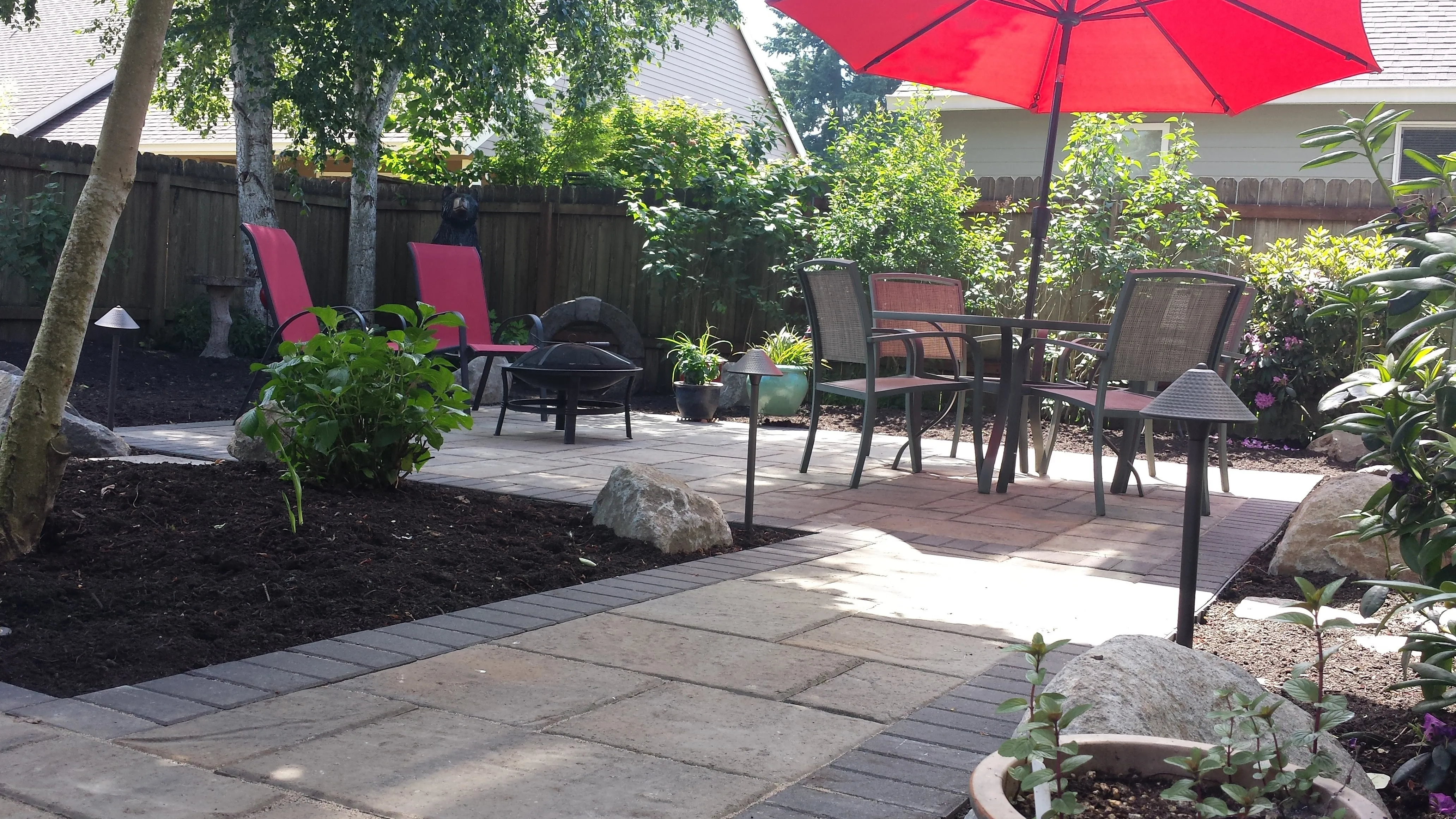 Paver patio with fire pit, dining set, and low-voltage path lights in a Canby backyard