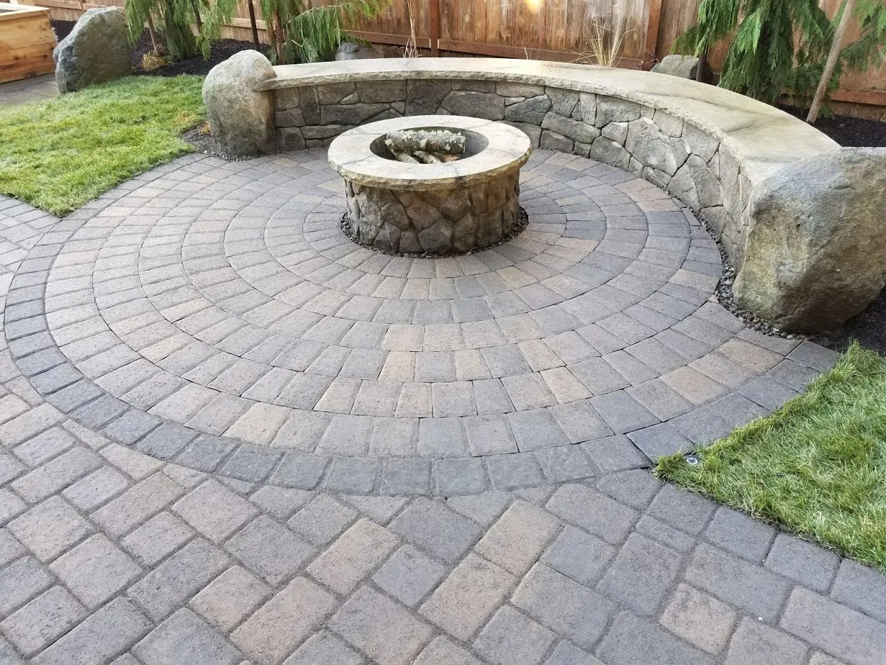Curved stone seat wall with boulder ends and a stone fire pit on a circular paver patio in Canby