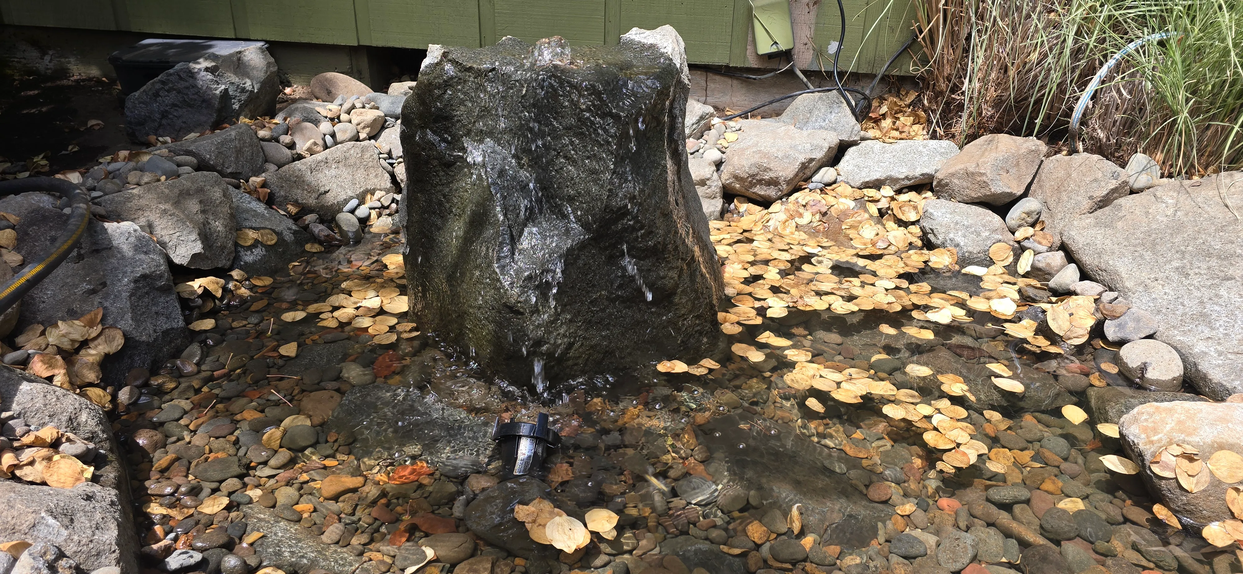 Basalt bubbler rock with water flowing over golden pebbles in a Canby garden