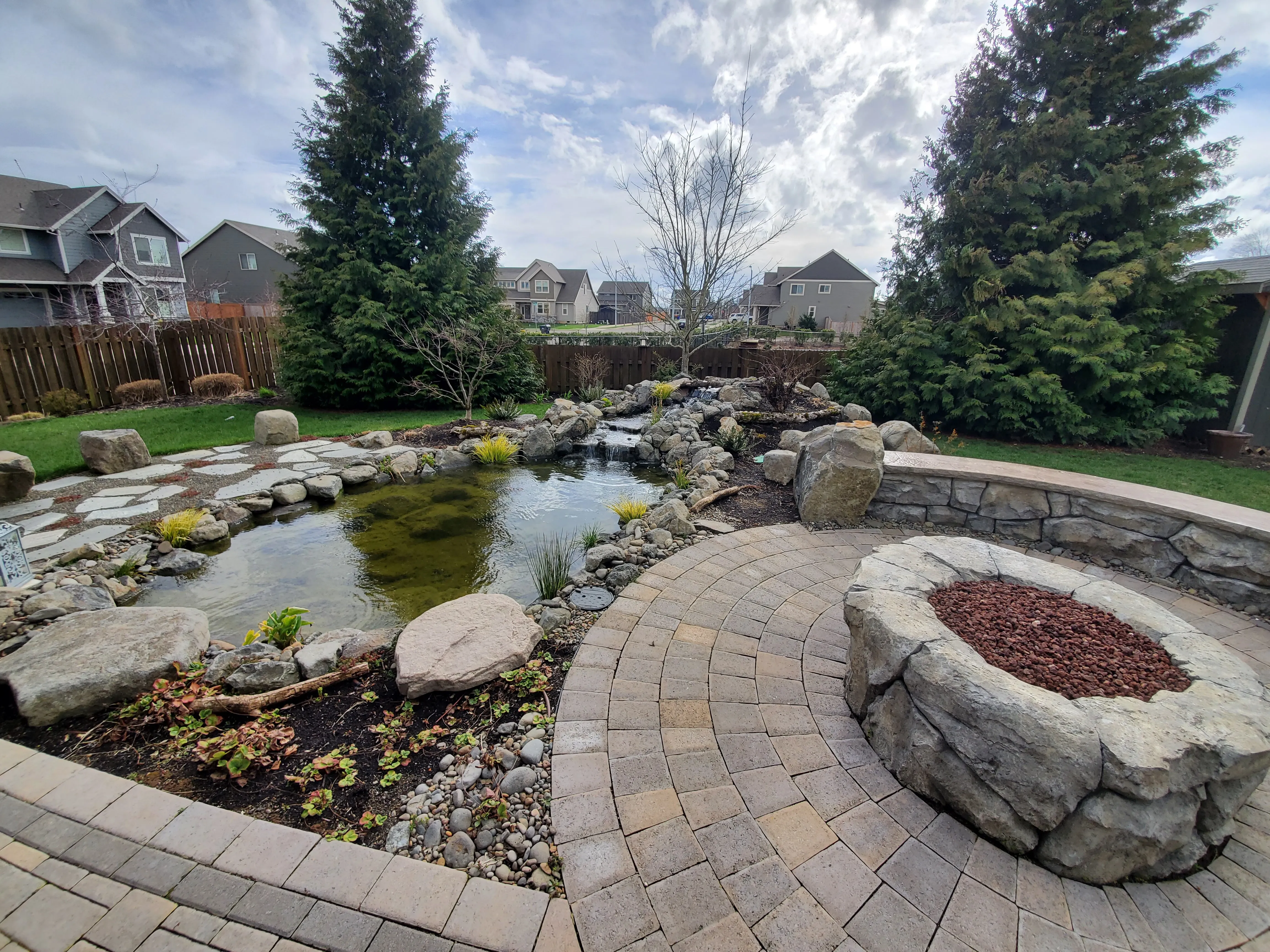 Backyard pond beside a paver patio and stone fire pit at an Oregon City home