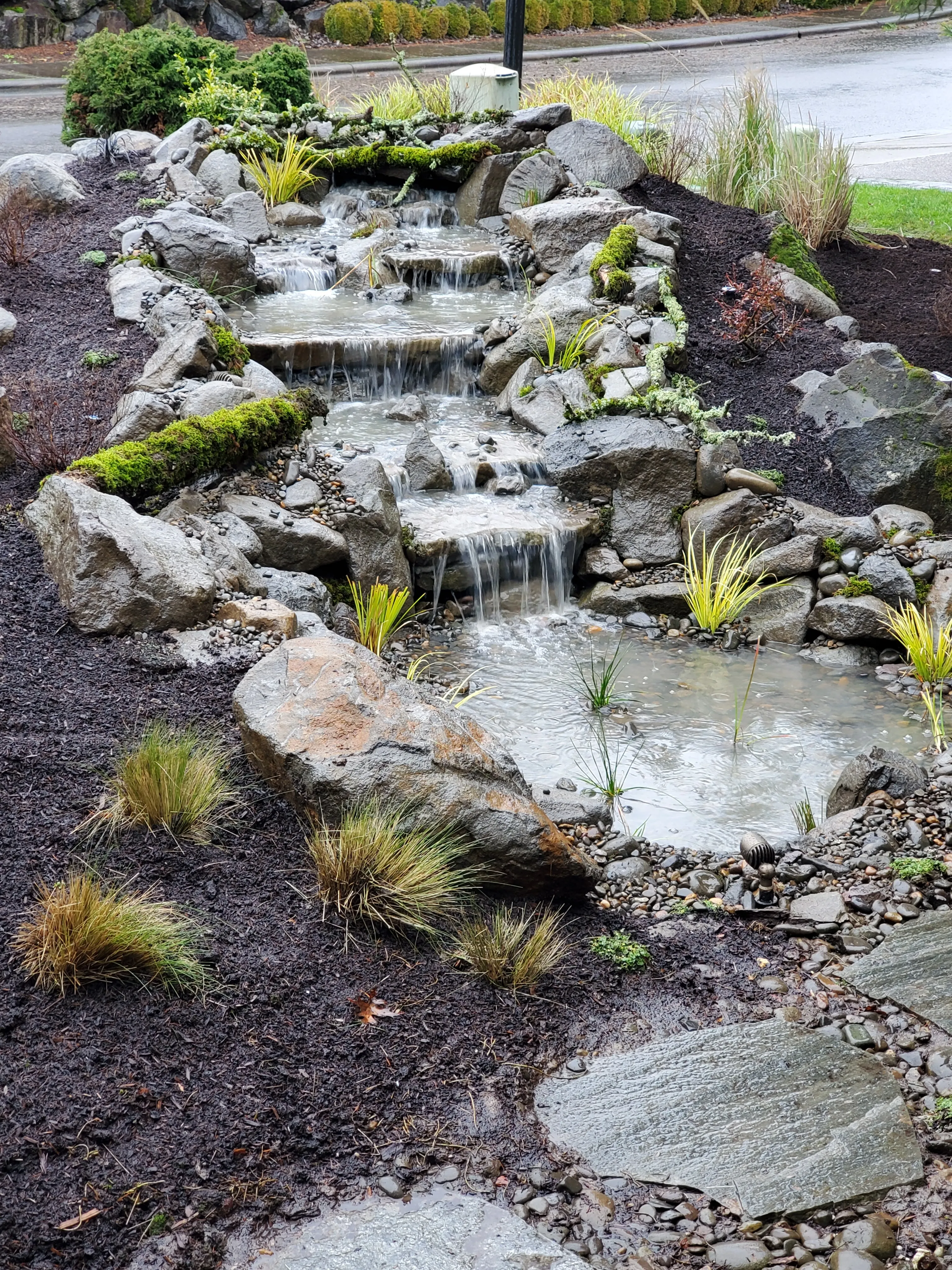 Rocky waterfall cascade feeding a river-rock stream at a Wilsonville home
