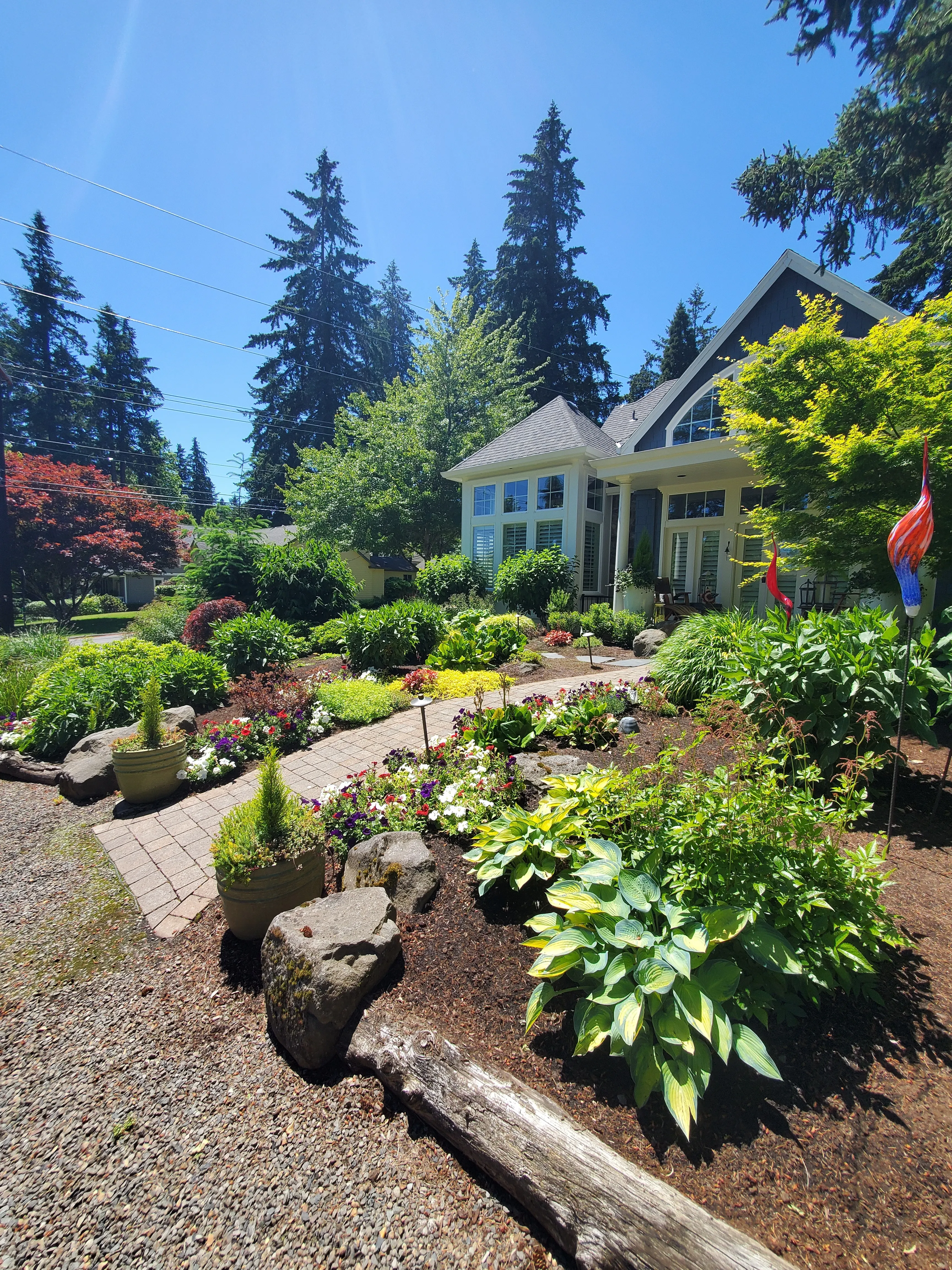 Front garden beds layered with shrubs, perennials, urns, and boulders