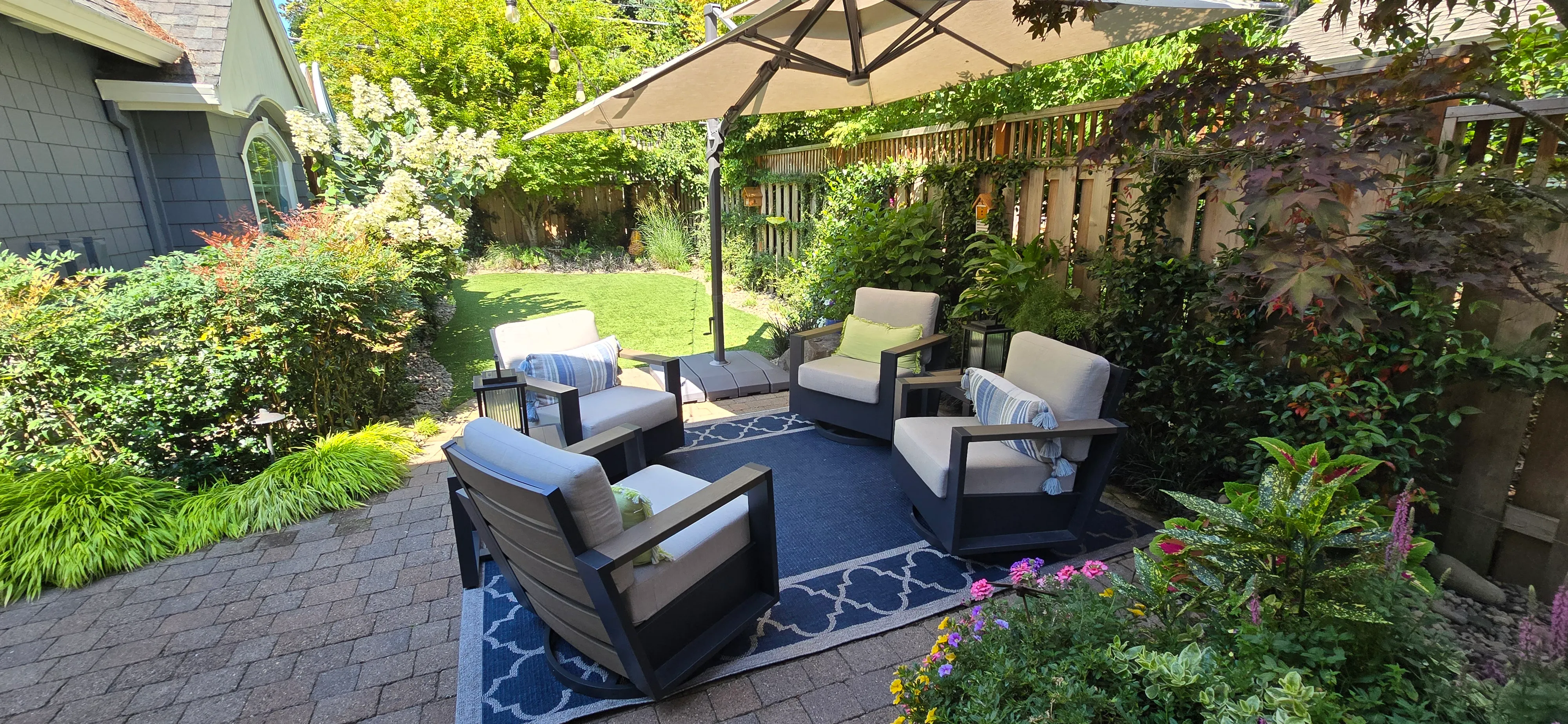 Outdoor seating area under an umbrella on the back patio, espaliered greenery trained along the fence