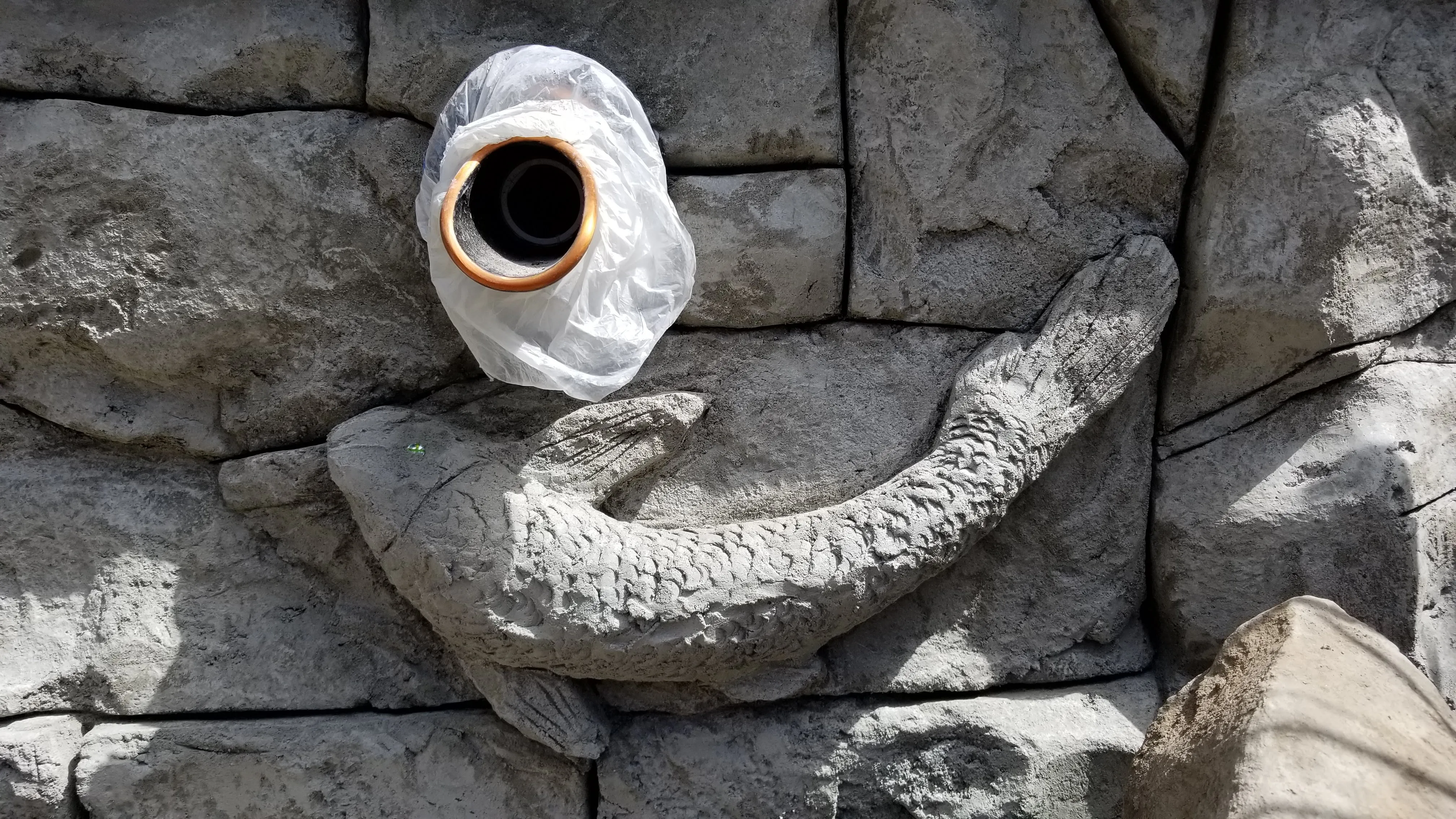 Raw hand-carved concrete koi curling around its wrapped spout before painting