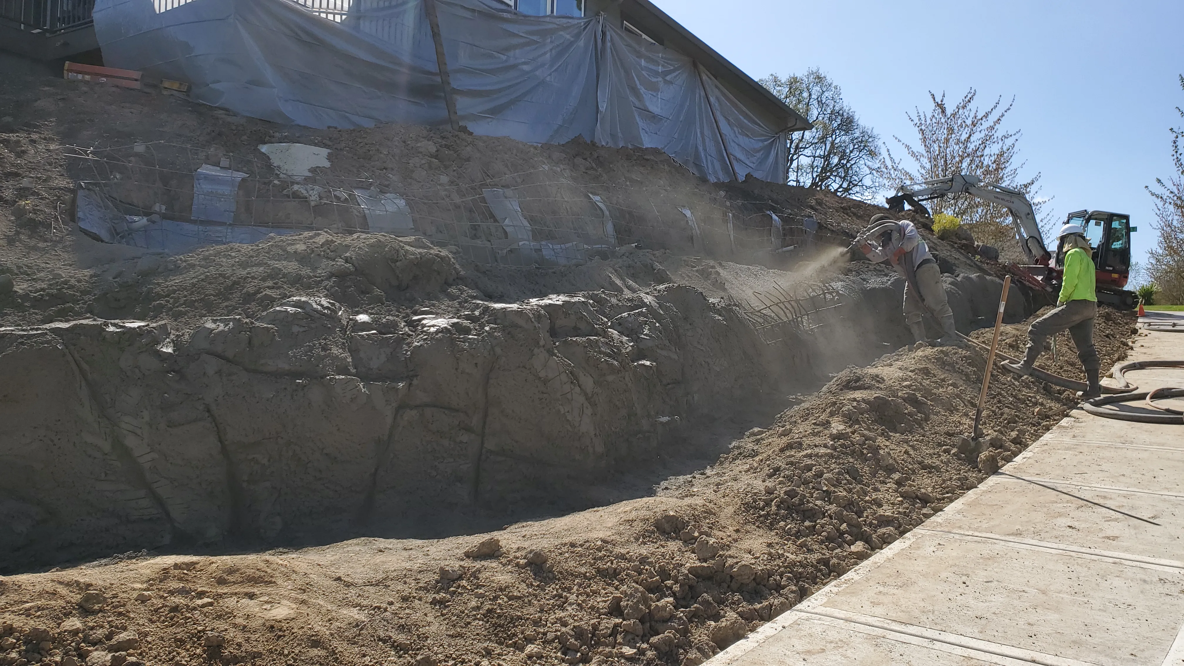 Fresh concrete being sprayed over the carved lower wall with the house wrapped above