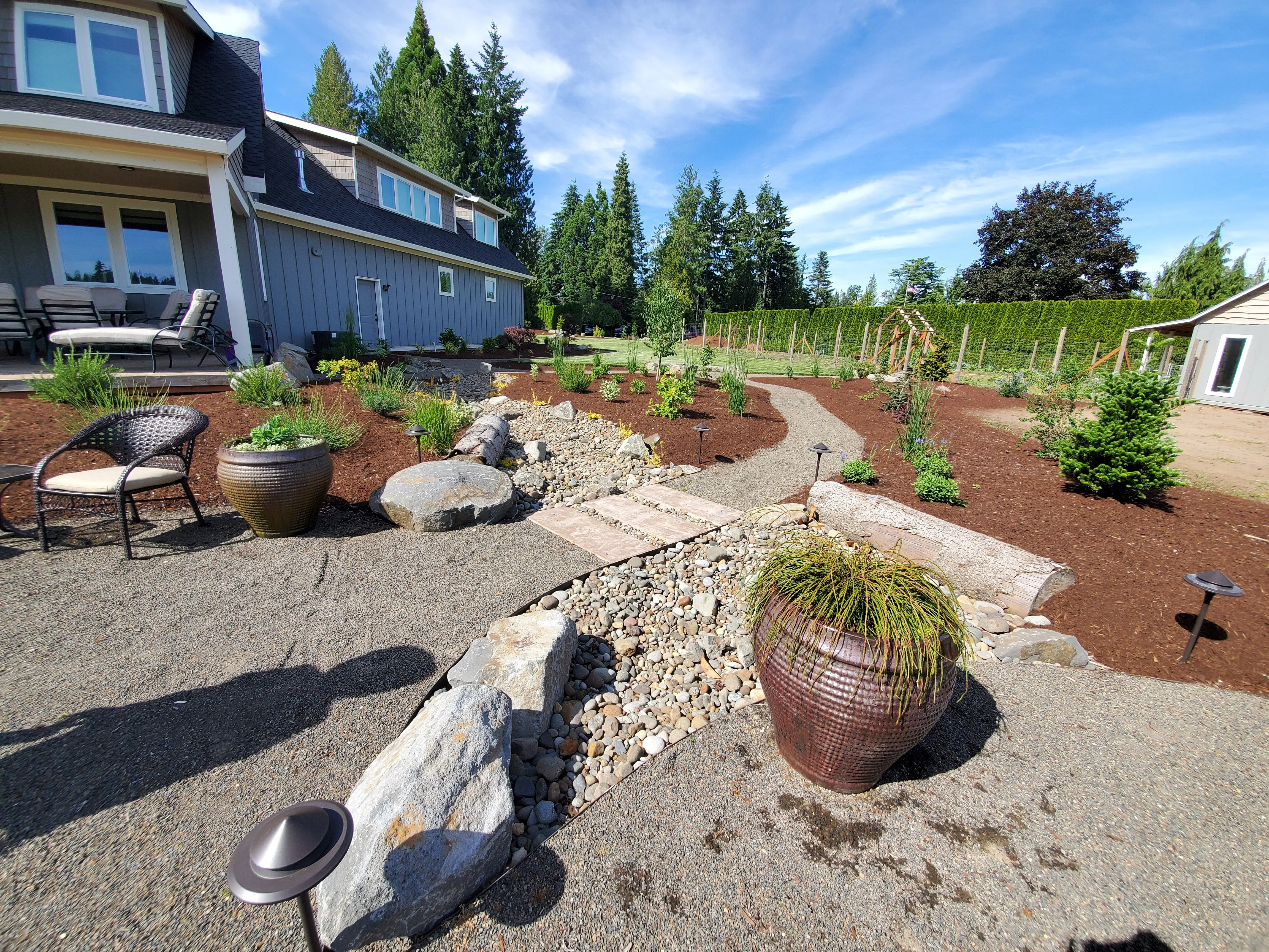 Gravel paths, river-rock drainage swale, and landscape lighting across a new Aurora yard