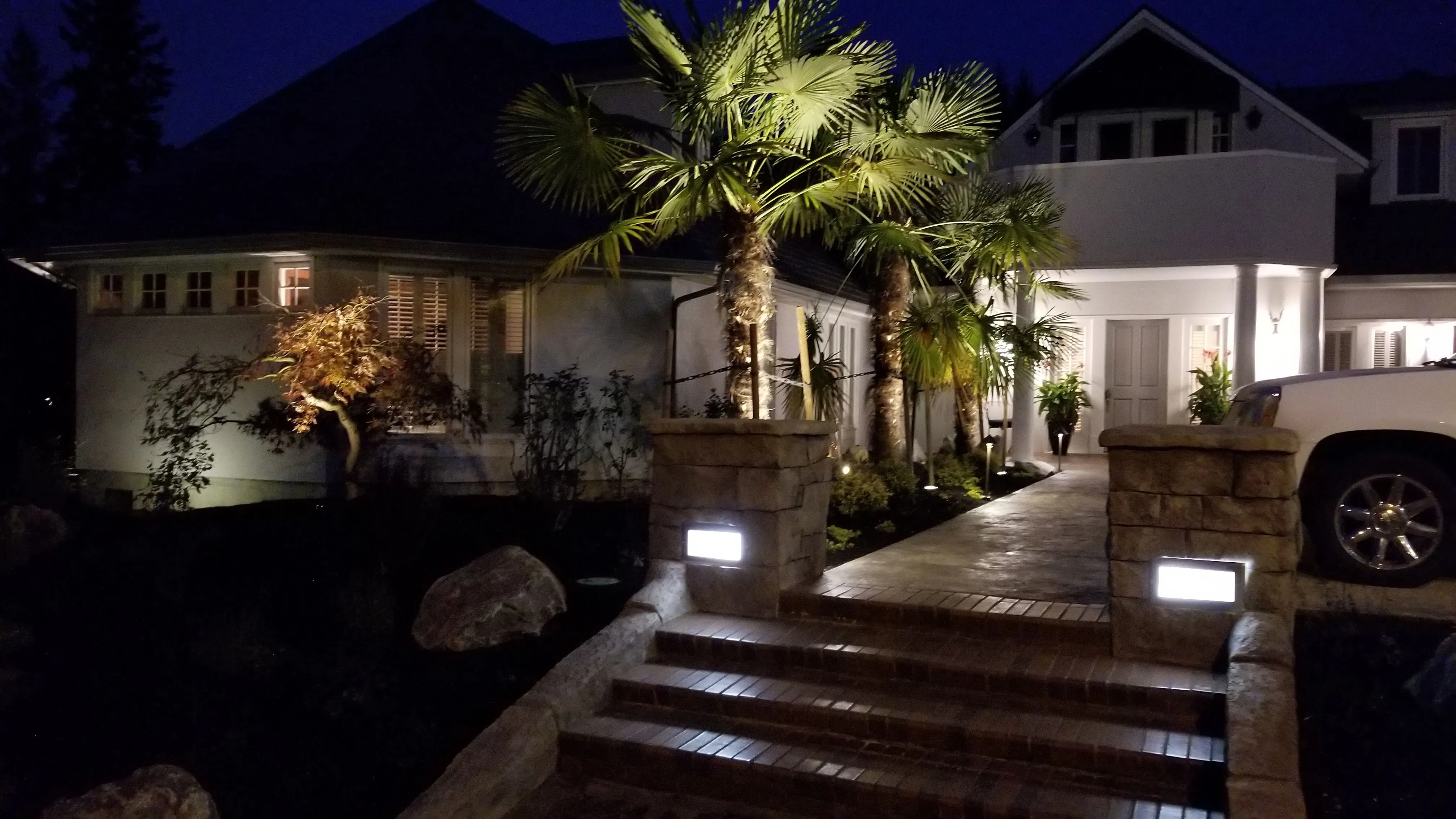 Low-voltage landscape lighting on palms, stone pillars, and an entry walk at a Charbonneau home at night
