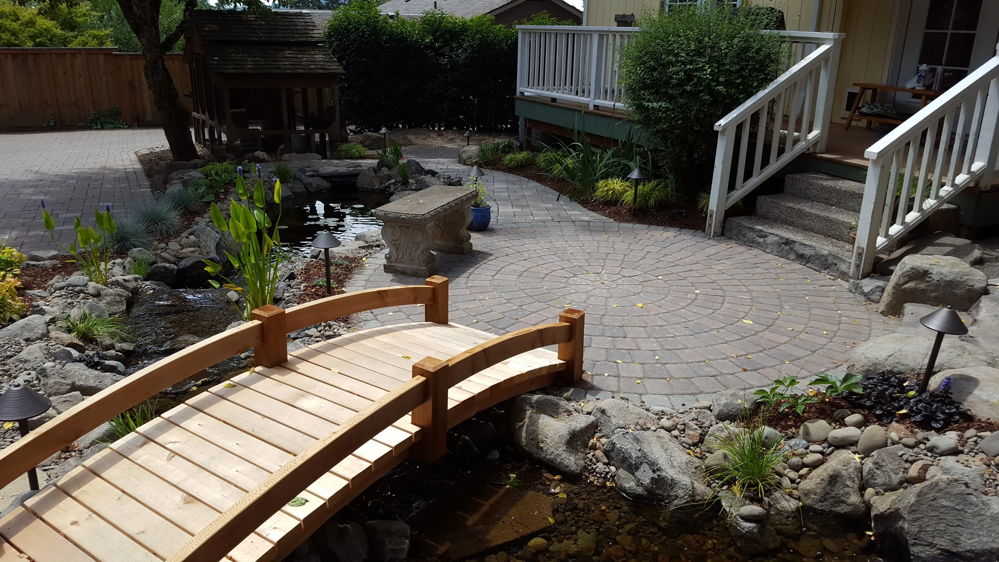 Cedar footbridge and circle paver patio over a stream garden at a Lake Oswego home