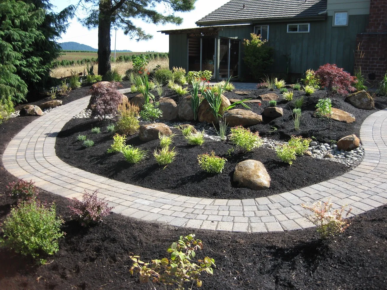 Double-bordered paver walkway sweeping around a bermed rock garden at an Oregon City property
