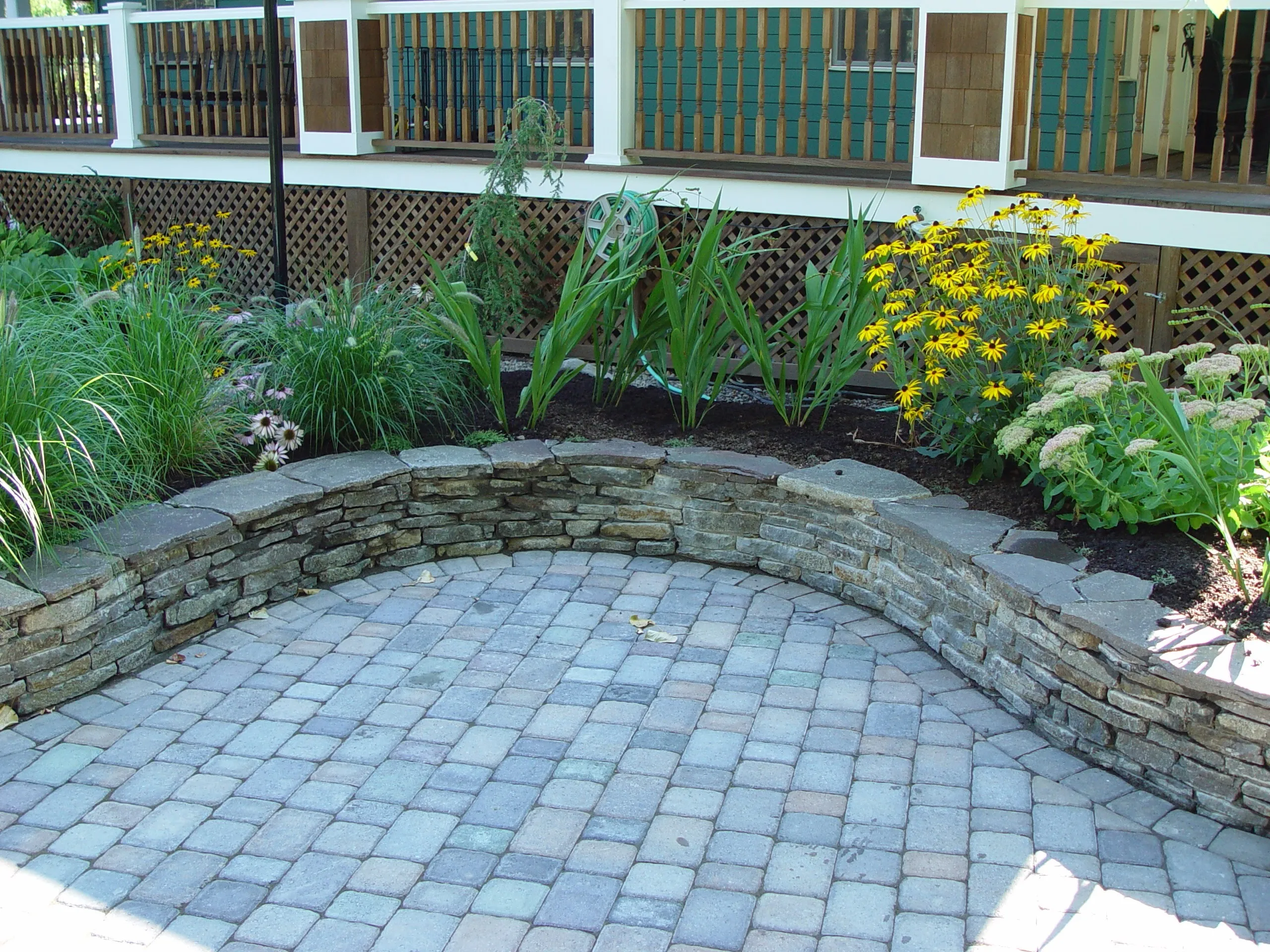 Dry-stacked stone wall curving around a circle paver patio with black-eyed Susans in Wilsonville